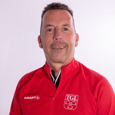 Eine lächelnder Mann trägt eine rote TGL-Jacke, symbolisierend den Sportgeist des Vereins Turngemeinde Landshut.