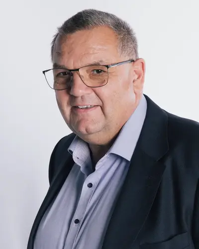 Sportleiter Jürgen Frank in Anzug und Brille lächelt freundlich, repräsentiert den Sportverein Turngemeinde Landshut.