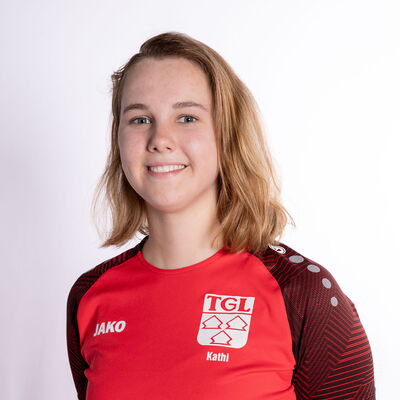 Eine lächelnde Frau in einem roten TGL-Sportshirt posiert vor einem weißen Hintergrund.