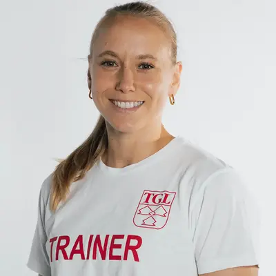 Eine Frau in einem T-Shirt mit "TGL Trainer" lächelt freundlich, repräsentierend den Sportverein Turngemeinde Landshut.
