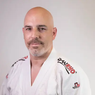 Ein Mann im weißen Judogi steht vor einem neutralen Hintergrund, möglicherweise ein Mitglied des Sportvereins Turngemeinde.