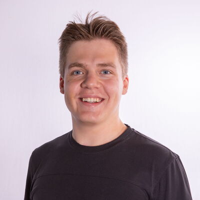 Ein lächelnder junger Mann in einem schwarzen T-Shirt steht vor einem neutralen Hintergrund, verbunden mit dem Sportverein Turngemeinde.