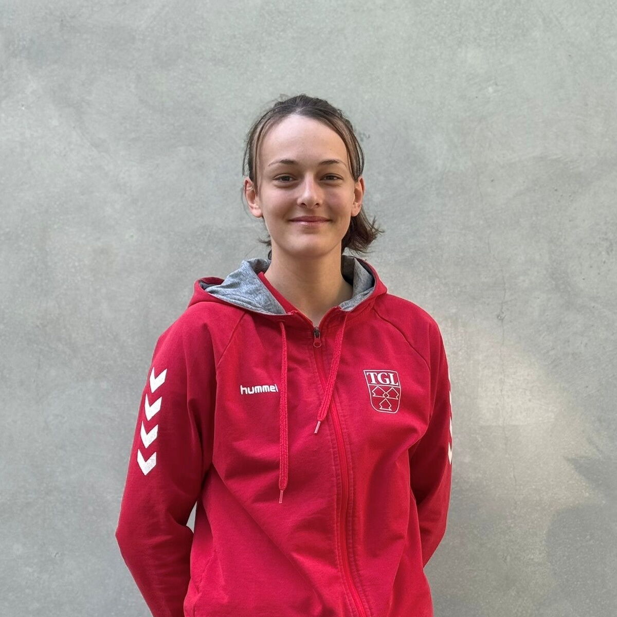 Eine junge Frau im roten TGL-Shirt lächelt freundlich in die Kamera, repräsentativ für den Verein in Landshut.