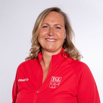 Eine lächelnde Frau trägt eine rote TGL-Jacke, symbolisierend den Sportgeist des Vereins Turngemeinde Landshut.
