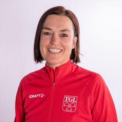 Eine lächelnde Frau trägt eine rote TGL-Jacke, symbolisierend den Sportgeist des Vereins Turngemeinde Landshut.