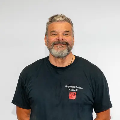 Ein lächelnder Mann trägt ein T-Shirt der Turngemeinde Landshut mit dem Logo des Vereins.