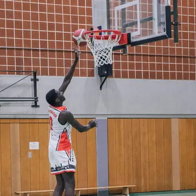 Ein Basketballspieler der Turngemeinde Landshut springt zum Korb und erzielt einen Punkt in der Sporthalle.