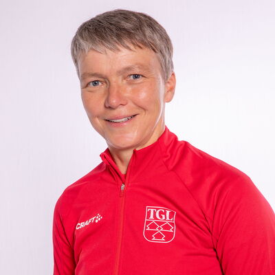 Eine lächelnde Frau trägt eine rote TGL-Jacke, symbolisierend den Sportgeist des Vereins Turngemeinde Landshut.