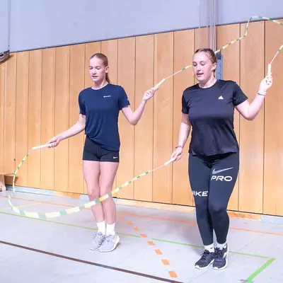 Zwei Frauen springen im Turnverein Landshut synchron mit bunten Springseilen in einer Turnhalle.