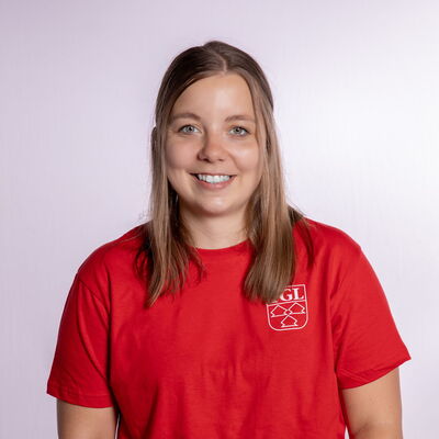 Eine Frau in einem roten TGL-Trikot lächelt in die Kamera, stolz ihren Sportverein Turngemeinde Landshut repräsentierend.