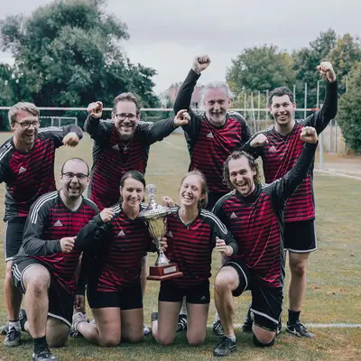 Ein jubelndes Sportteam der Turngemeinde Landshut feiert mit einem Pokal auf dem Sportplatz.