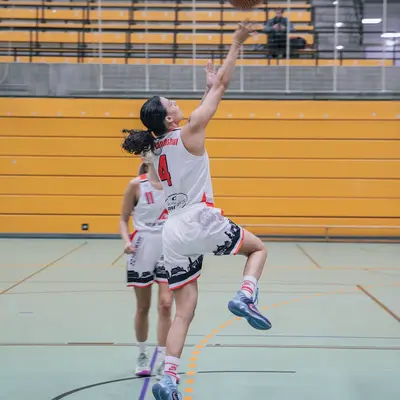 Ein Basketballspieler des Vereins Landshut springt dynamisch zum Korb für einen erfolgreichen Layup im Spiel.