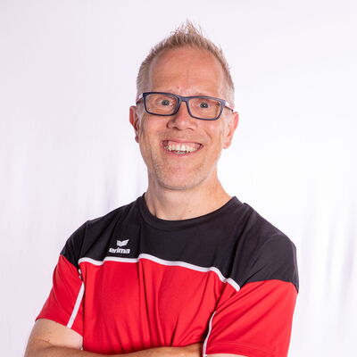 Ein Mann in Sportkleidung lächelt mit verschränkten Armen, repräsentierend den Verein Turngemeinde Landshut.