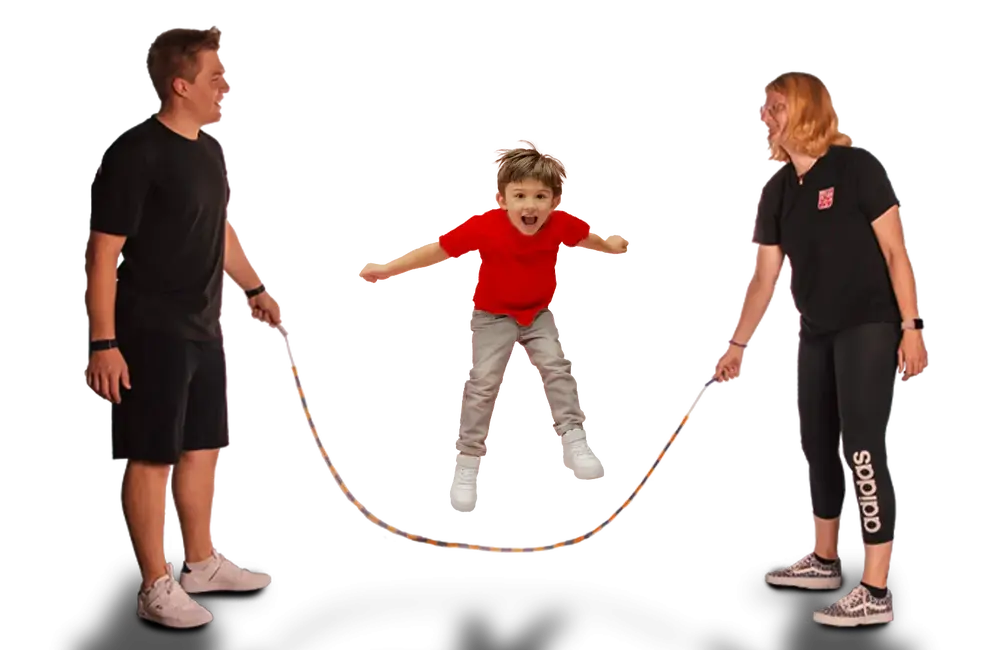 Ein Kind springt begeistert Seil zwischen zwei Erwachsenen bei einer Sportaktivität des Vereins Turngemeinde Landshut.