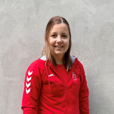 Eine Frau in einem roten TGL-Shirt der Turngemeinde Landshut lächelt vor einem neutralen Hintergrund.