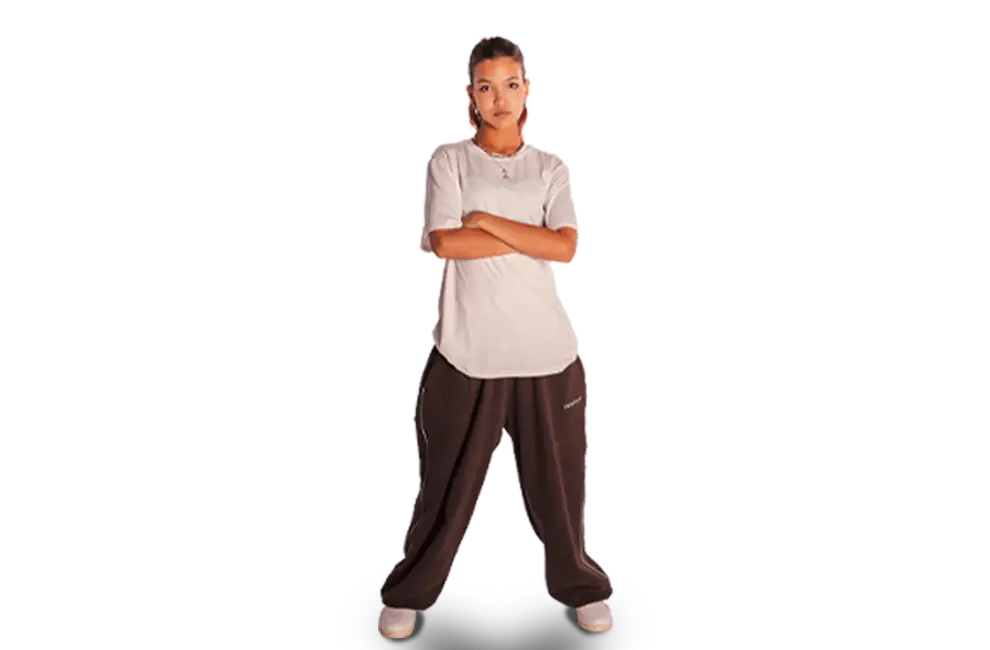 Eine junge Frau in lässiger Hip-Hop-Kleidung steht selbstbewusst mit verschränkten Armen, ideal für den Sportverein TGL.