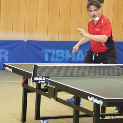 Ein Tischtennisspieler in rotem Trikot konzentriert sich beim Turnier der Turngemeinde Landshut auf seinen nächsten Schlag.