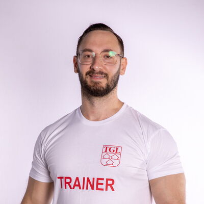 Ein Trainer der Turngemeinde Landshut steht in einem TGL-T-Shirt und lächelt in die Kamera.