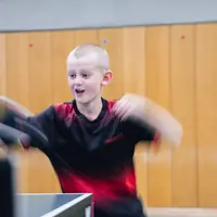 Ein Junge in rotem Trikot spielt Tischtennis im Verein Turngemeinde Landshut.