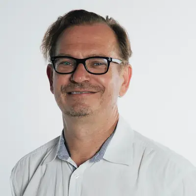 Ein Mann in einem weißen Hemd lächelt freundlich, möglicherweise ein Mitglied des Sportvereins Turngemeinde Landshut.