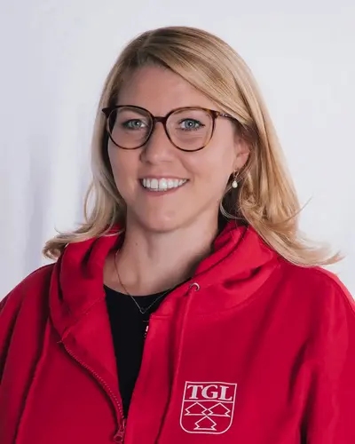 Eine Frau in rotem TGL-Pullover lächelt freundlich und repräsentiert den Sportverein Turngemeinde Landshut.