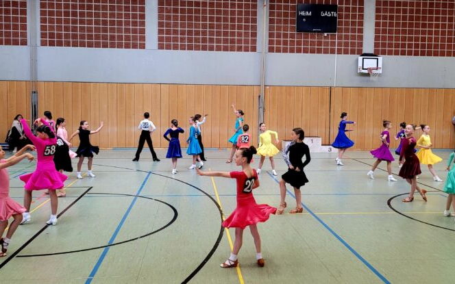 In einer Sporthalle tanzen Kinder in bunten Kleidern bei einer Veranstaltung der Turngemeinde Landshut.