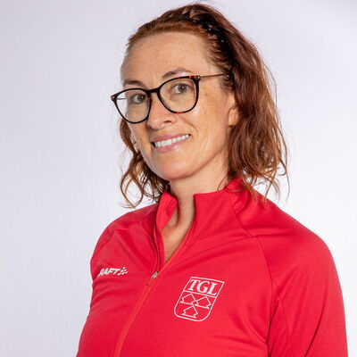 Eine lächelnde Frau trägt eine rote TGL-Jacke, symbolisierend den Sportgeist des Vereins Turngemeinde Landshut.