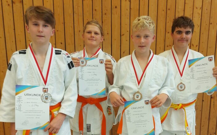 Vier junge Judoka der Turngemeinde Landshut zeigen stolz ihre Medaillen und Urkunden nach einem erfolgreichen Wettkampf.