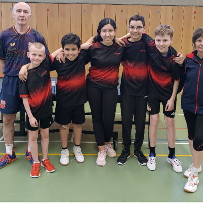 Eine Gruppe Tischtennisspieler der Turngemeinde Landshut posiert fröhlich vor einem Tisch im Sportverein.