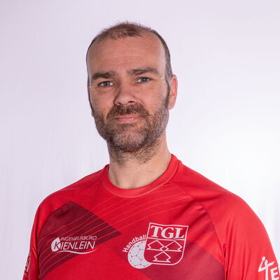 Ein Mann im roten Trikot der TGL-Handballmannschaft lächelt freundlich in die Kamera.