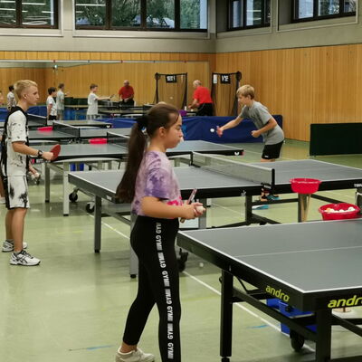 Kinder trainieren Tischtennis in der Halle des Sportvereins Turngemeinde Landshut, betreut von einem Erwachsenen.