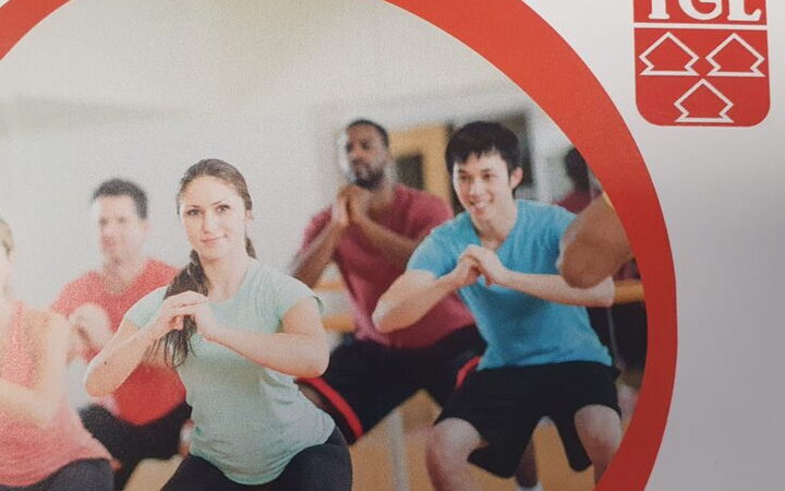 Eine Gruppe von Menschen macht Fitnessübungen im Vereinszentrum der Turngemeinde Landshut, erkennbar am TGL-Logo.