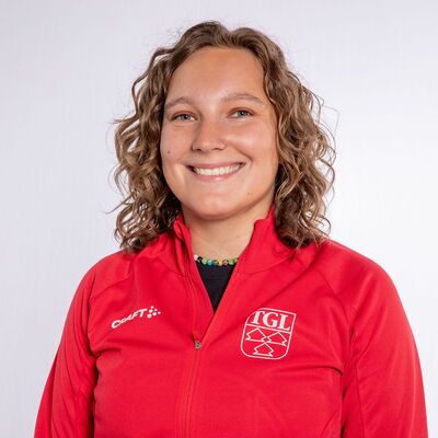 Eine lächelnde Frau trägt eine rote TGL-Jacke, symbolisierend den Sportgeist des Vereins Turngemeinde Landshut.