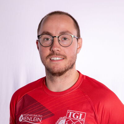 Ein Handballspieler der Turngemeinde Landshut trägt ein rotes TGL-Trikot und lächelt in die Kamera.
