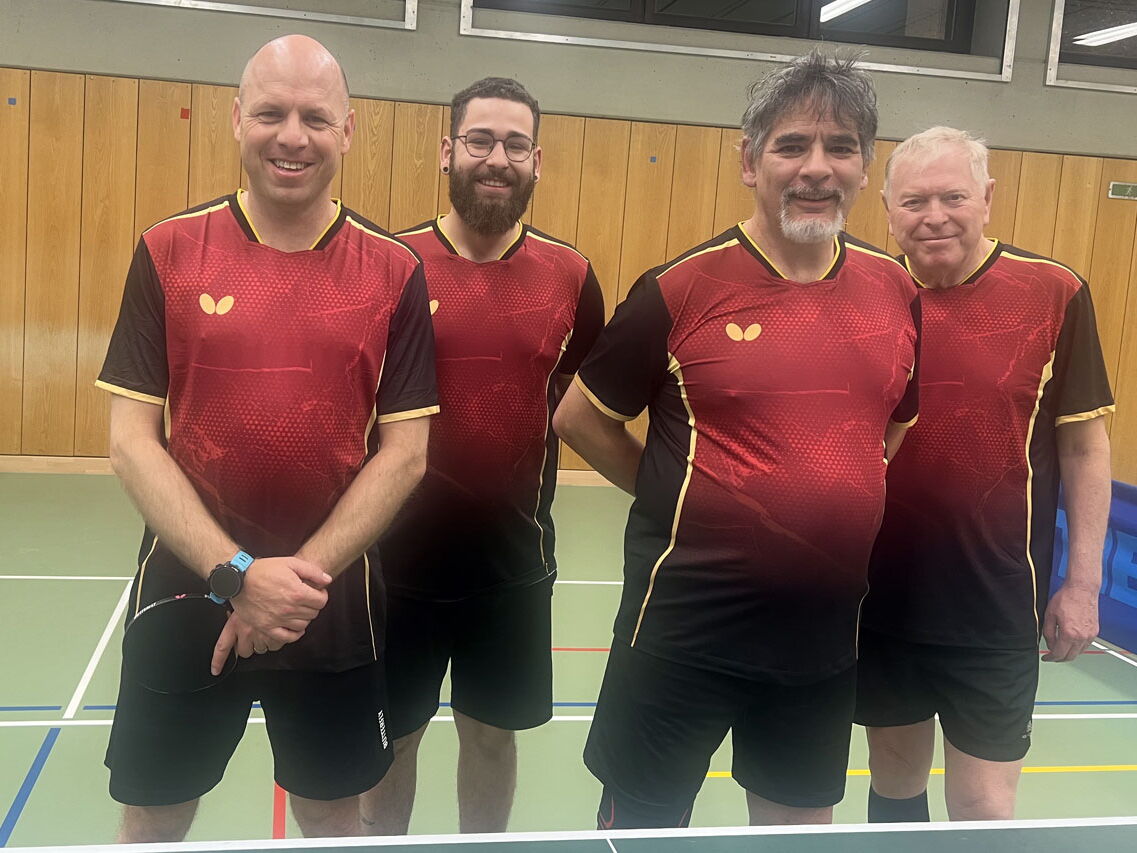 Vier Männer im einheitlichen Sporttrikot posieren in einer Sporthalle der Turngemeinde Landshut für ein Teamfoto.