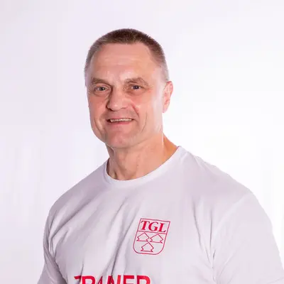 Ein lächelnder Trainer im TGL-Shirt steht vor einem neutralen Hintergrund, repräsentiert den Sportverein.
