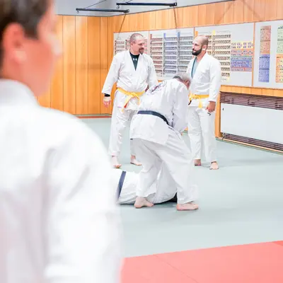 Judokas der Turngemeinde Landshut üben im Dojo, während ein Trainer Anweisungen gibt.