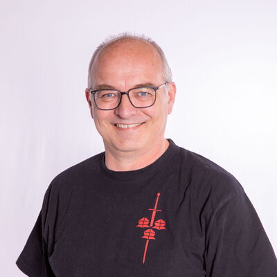 Ein lächelnder Mann mit Brille trägt ein T-Shirt mit Fechtmotiv, repräsentierend die Turngemeinde Landshut.