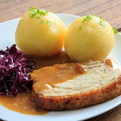 Ein traditionelles bayerisches Gericht mit Schweinebraten, Knödeln und Rotkohl auf einem Teller, ideal nach dem Sport im Verein.