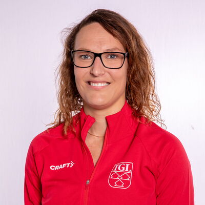 Eine lächelnde Frau trägt eine rote TGL-Jacke, symbolisierend den Sportgeist des Vereins Turngemeinde Landshut.