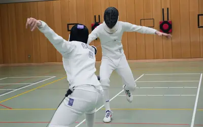 Zwei Fechter der Turngemeinde Landshut üben in voller Montur einen dynamischen Angriff auf der Sporthalle.
