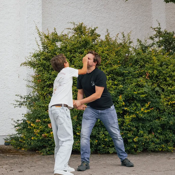 Ein junger Mann und ein Kind üben Selbstverteidigungstechniken im Freien beim Sportverein Turngemeinde Landshut.