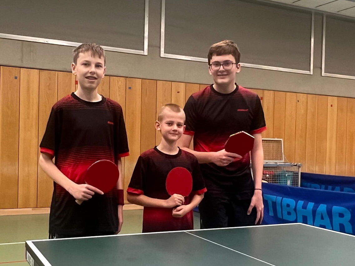 Drei junge Tischtennisspieler der Turngemeinde Landshut posieren stolz mit Schlägern in der Sporthalle des Vereins.