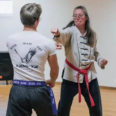 Zwei Personen üben Kung Fu in einem Sportraum der Turngemeinde Landshut, wobei eine Frau einen Schlag ausführt.
