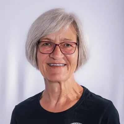 Eine Frau mit grauem Haar und Brille lächelt in einem T-Shirt der Turngemeinde Landshut.