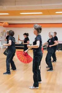Frauen der Turngemeinde Landshut üben im Vereinssaal mit bunten Fächern eine Tanzroutine.
