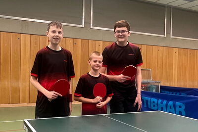 Drei junge Tischtennisspieler der Turngemeinde Landshut posieren stolz mit Schlägern in der Sporthalle des Vereins.