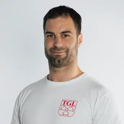 Ein lächelnder Trainer im TGL-Shirt steht vor einem neutralen Hintergrund, repräsentiert den Sportverein.