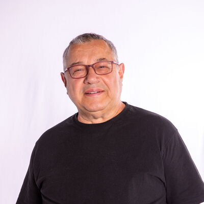 Ein älterer Mann in schwarzem T-Shirt lächelt freundlich in die Kamera und symbolisiert den Geist der Turngemeinde Landshut.