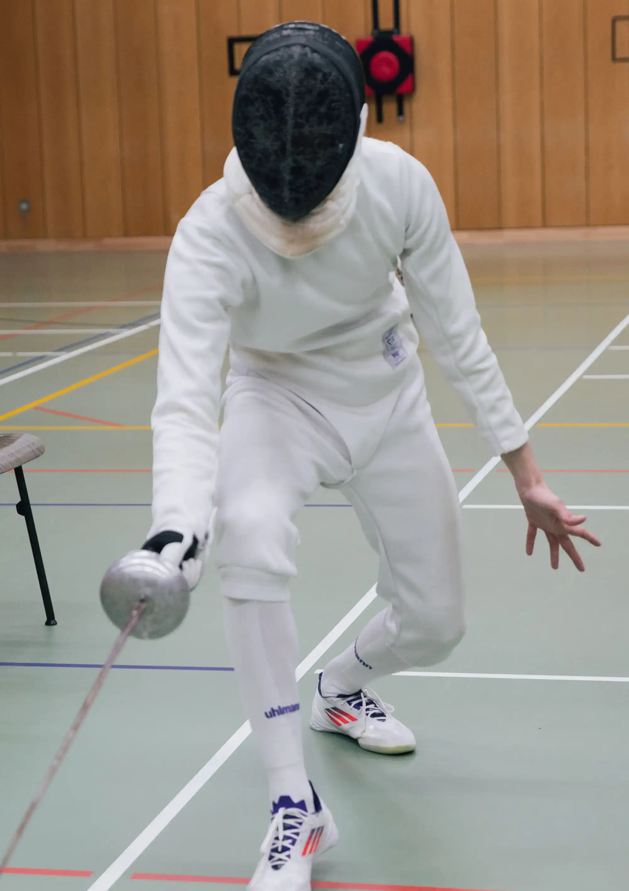 Ein Fechter im weißen Anzug führt einen Ausfallschritt in einer Turnhalle der Turngemeinde Landshut aus.